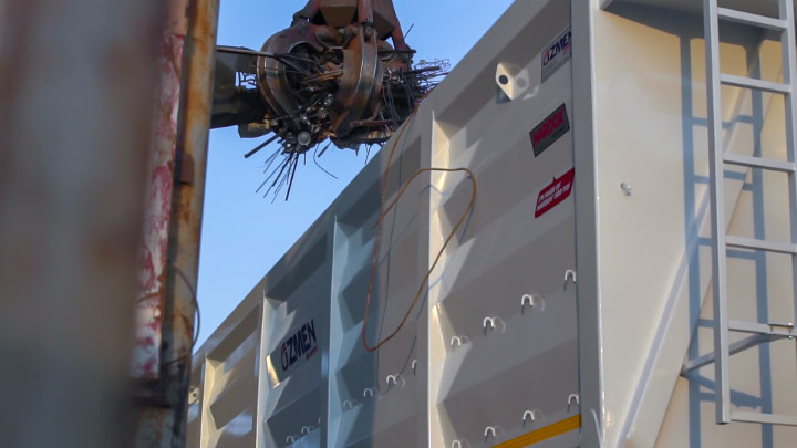 The new Özmen Damper recycling trailer is being loaded with metal scrap by a grapple. 